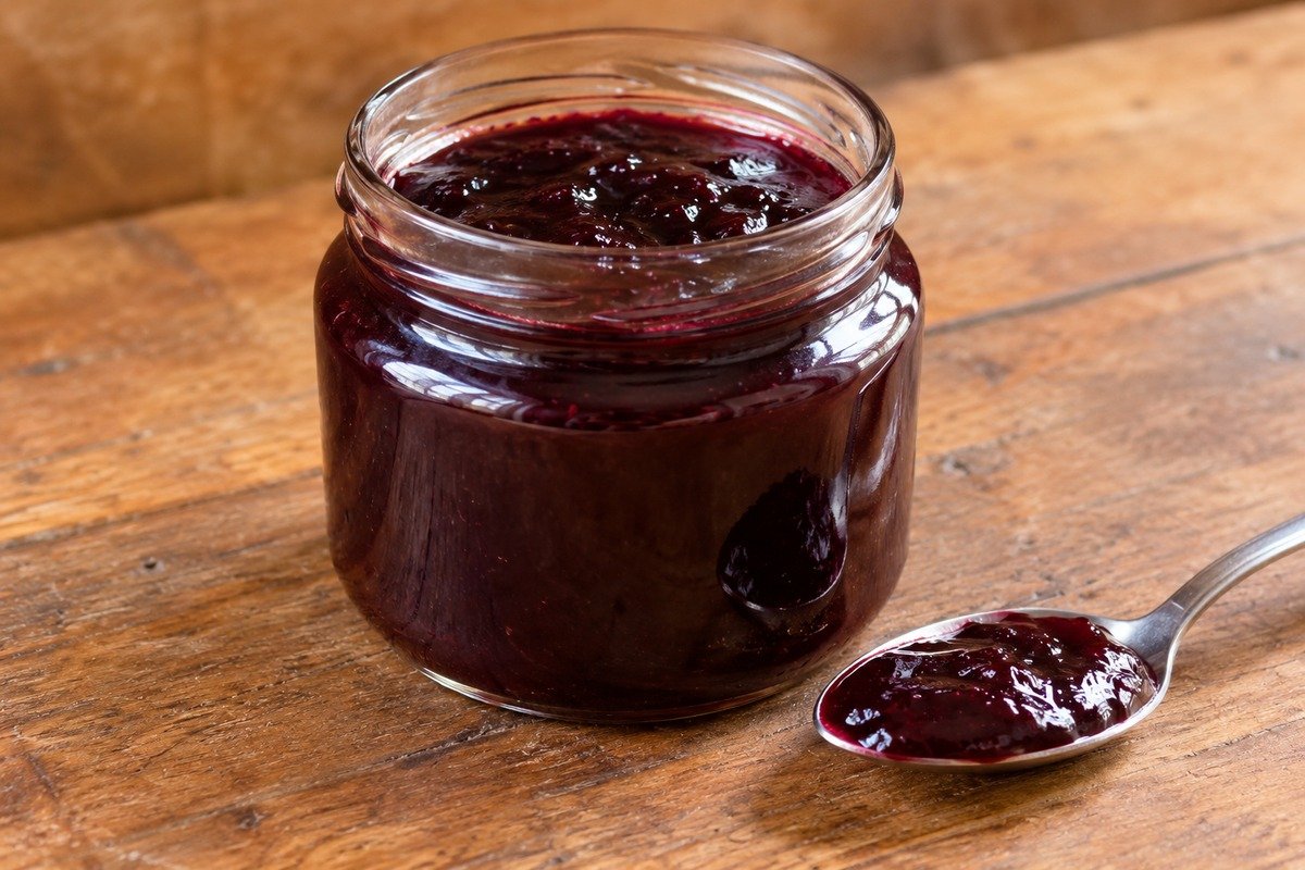 Geleia de jabuticaba roxa escura e brilhante em pote de vidro, com pequena porção em uma colher.