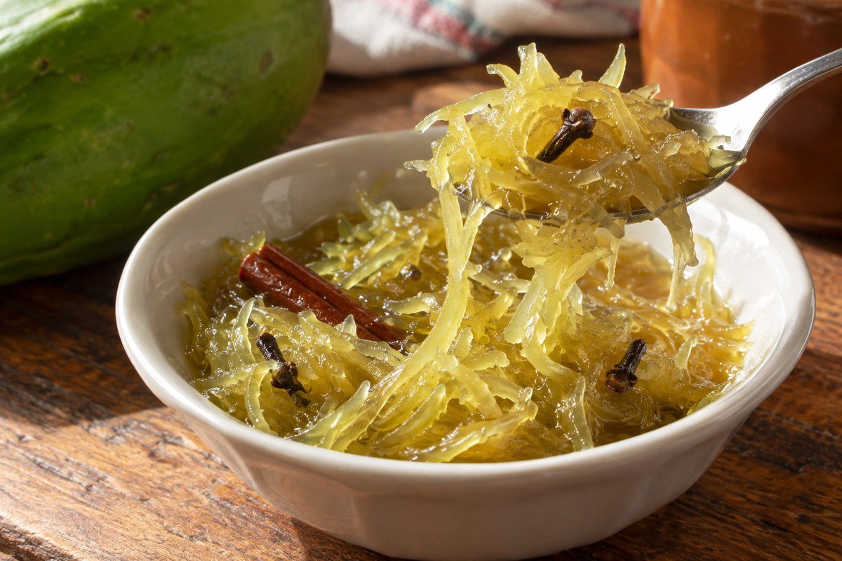 Doce de mamão verde ralado em fios brilhantes, com colher, cravo e canela.